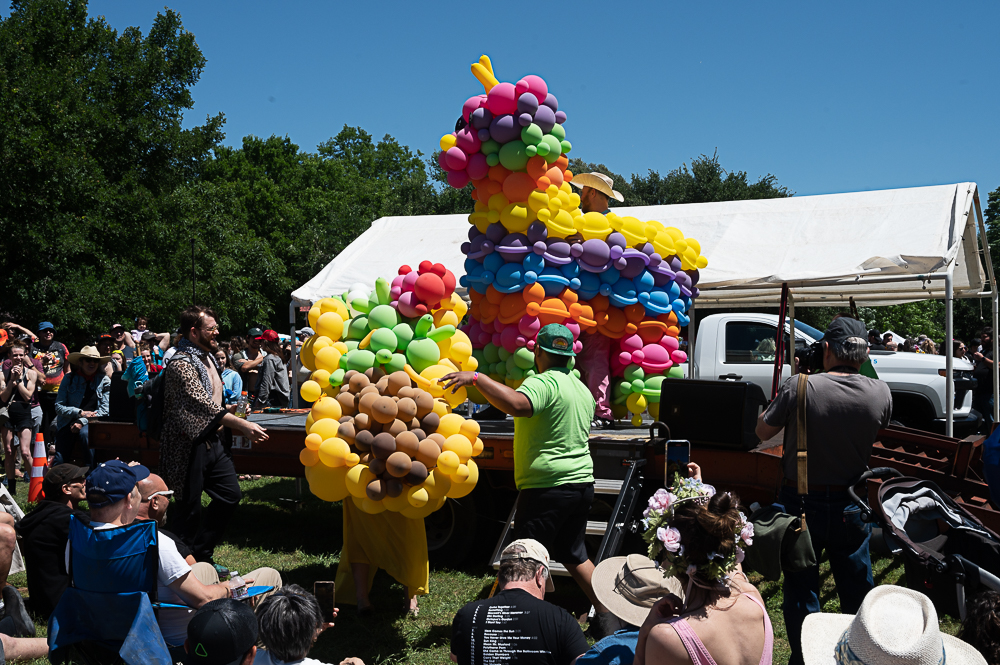 The stage at Eeyore's Birthday (2023) being set up with two large pieces of balloon art; a large colorful donkey and a taco, amidst a group of party attendees.  