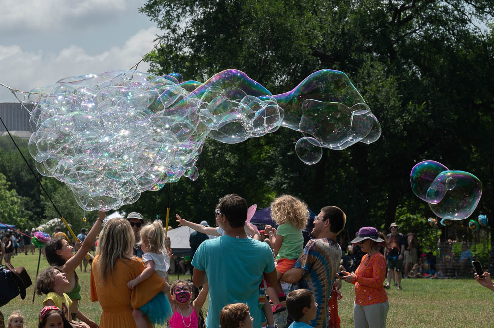 Children and adults gather, delighted by large, iridescent soap bubbles floating in the air at Eeyore's.