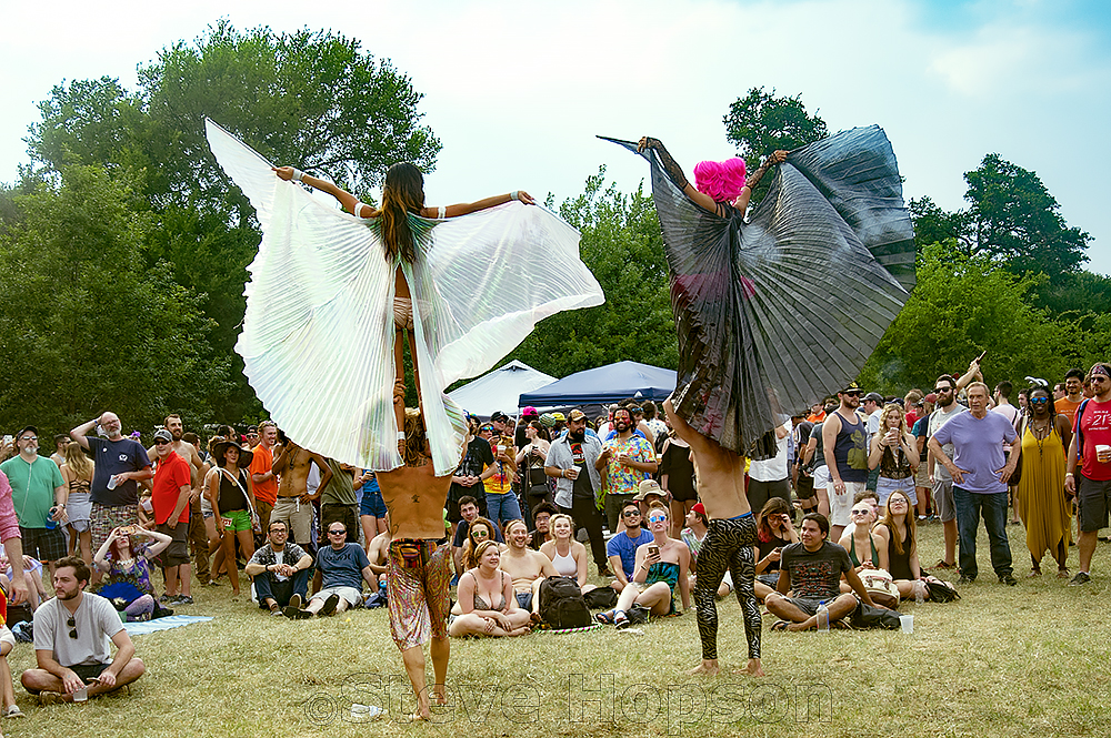 Two performers balance on the shoulders of two other performers while wearing flowing capes, entertaining a large crowd Eeyore's.